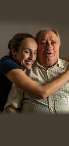 Femme d’âge moyen qui sourit et serre dans ses bras un homme âgé pour illustrer « Selma et Mohamed ».