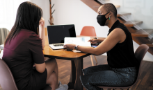 Femme face à un écran d’ordinateur qui tient un dossier et parle à une autre femme, pour illustrer le règlement alternatif de différends.